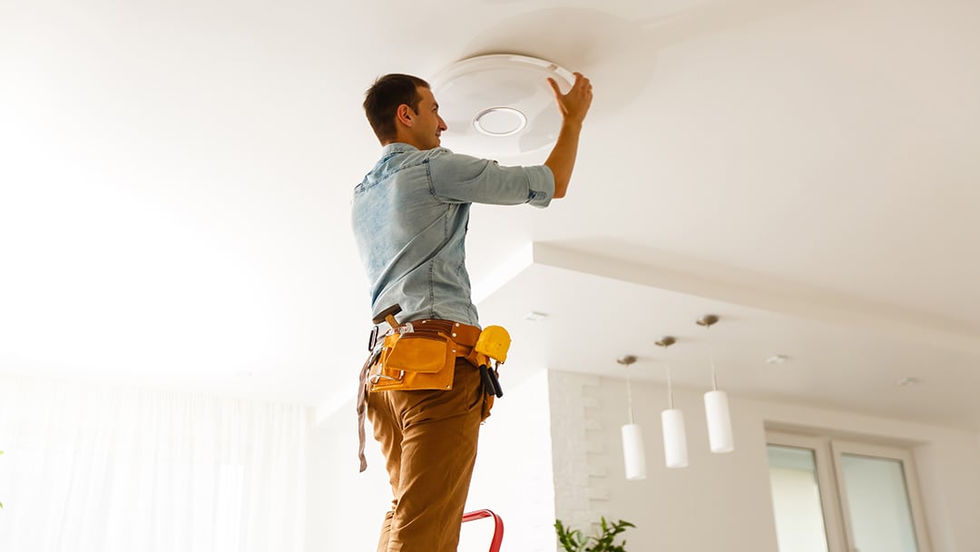 Handwerker steht auf einer Leiter und installiert eine Lampe an der Decke in einem modernen Wohnraum.